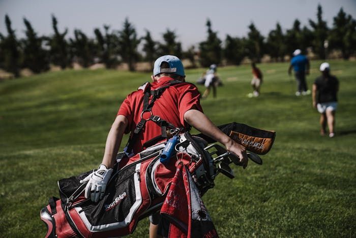 Golfer carrying bag with group on fairway